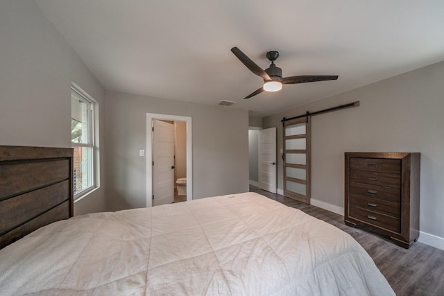 bedroom featuring a barn door, ceiling fan, dark wood-type flooring, and connected bathroom