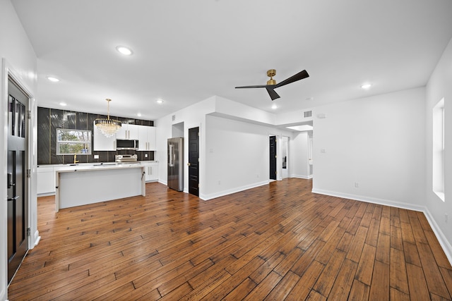 unfurnished living room featuring ceiling fan with notable chandelier and hardwood / wood-style flooring