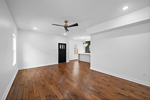 unfurnished living room featuring ceiling fan with notable chandelier and dark hardwood / wood-style flooring