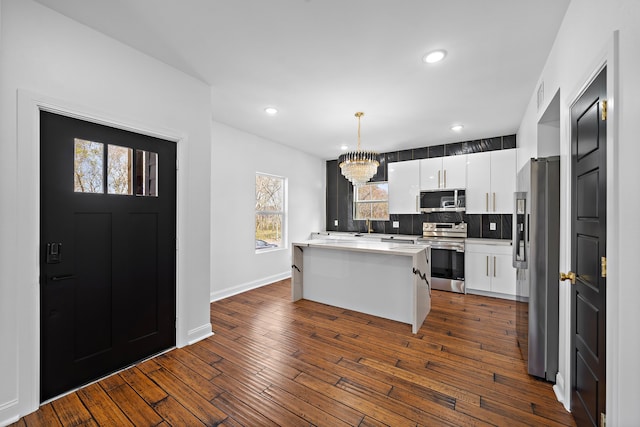 kitchen featuring tasteful backsplash, decorative light fixtures, a kitchen island, white cabinetry, and stainless steel appliances