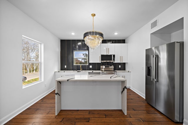 kitchen with stainless steel appliances, decorative light fixtures, a notable chandelier, white cabinets, and a kitchen island