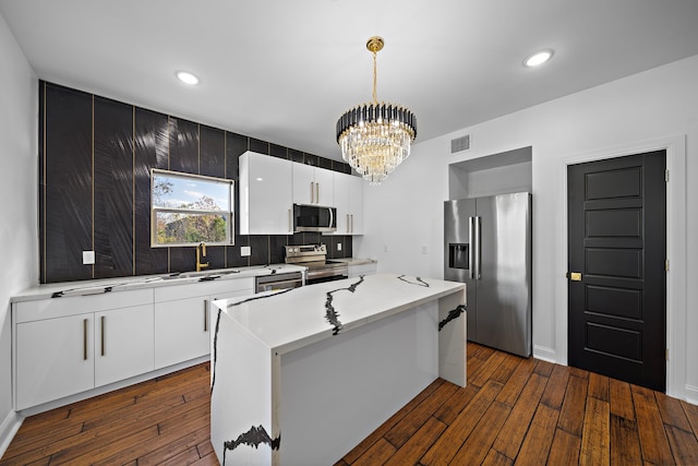 kitchen with white cabinetry, stainless steel appliances, a chandelier, decorative light fixtures, and a kitchen island