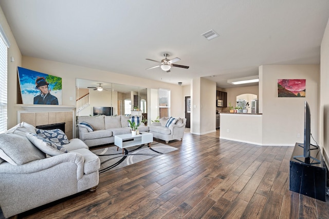 living room featuring a tiled fireplace, ceiling fan, and dark hardwood / wood-style flooring