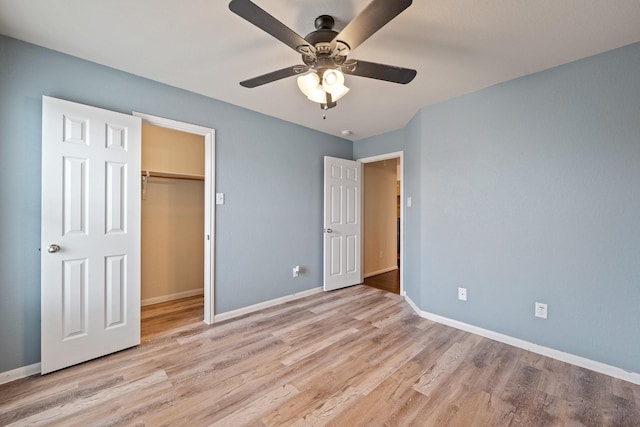 unfurnished bedroom featuring a walk in closet, a closet, ceiling fan, and light hardwood / wood-style floors