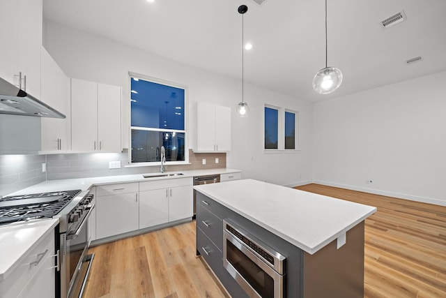 kitchen featuring stainless steel range, sink, decorative light fixtures, a center island, and white cabinetry