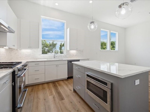 kitchen featuring light wood-type flooring, stainless steel appliances, sink, a center island, and white cabinetry