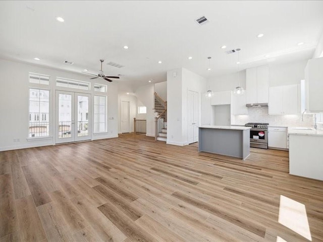 kitchen with a center island, hanging light fixtures, light wood-type flooring, stainless steel range oven, and white cabinetry