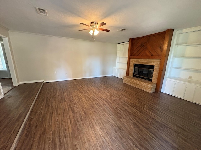 unfurnished living room with dark wood-type flooring, ceiling fan, built in shelves, a textured ceiling, and a fireplace