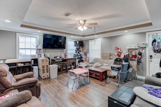 living room with ceiling fan, light wood-type flooring, crown molding, and a tray ceiling