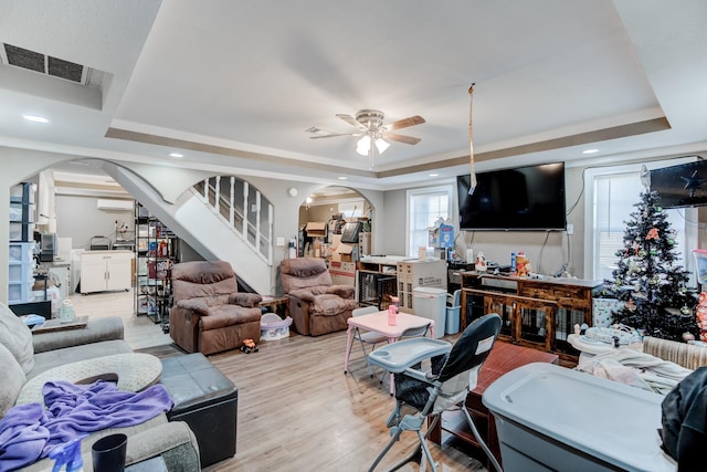 living room with a raised ceiling, ceiling fan, light hardwood / wood-style flooring, and an AC wall unit