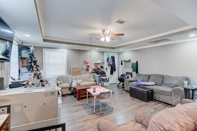 living room with a raised ceiling, ceiling fan, and light hardwood / wood-style flooring