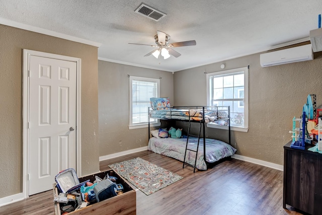 bedroom with multiple windows, hardwood / wood-style flooring, a wall unit AC, and ceiling fan