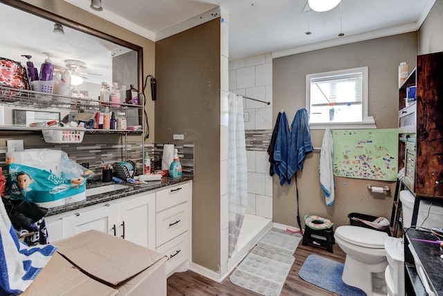 bathroom with toilet, wood-type flooring, a tile shower, and ornamental molding