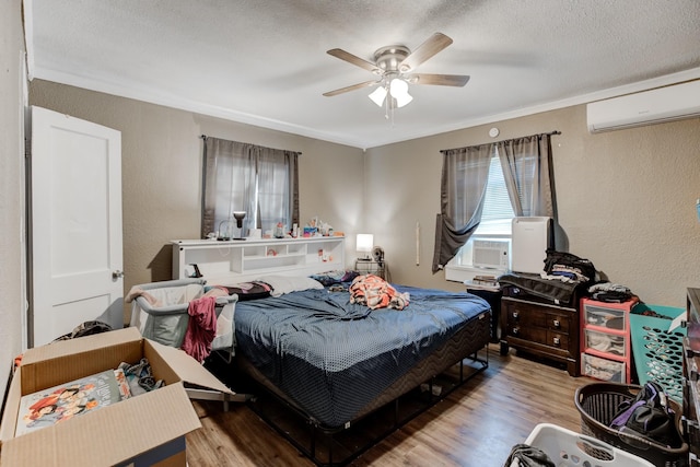 bedroom with a wall mounted air conditioner, ceiling fan, light wood-type flooring, and a textured ceiling