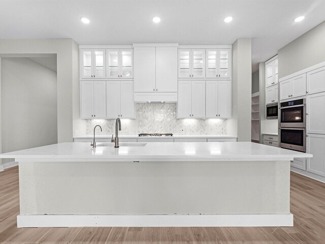 kitchen featuring a large island with sink, white cabinets, light wood-type flooring, and appliances with stainless steel finishes