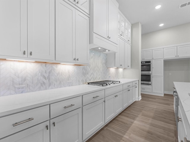 kitchen featuring light stone counters, light hardwood / wood-style flooring, stainless steel appliances, decorative backsplash, and white cabinetry