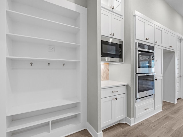 kitchen featuring backsplash, stainless steel appliances, light hardwood / wood-style floors, and white cabinets