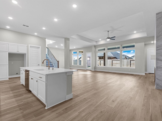 kitchen with sink, an island with sink, white cabinets, and a tray ceiling