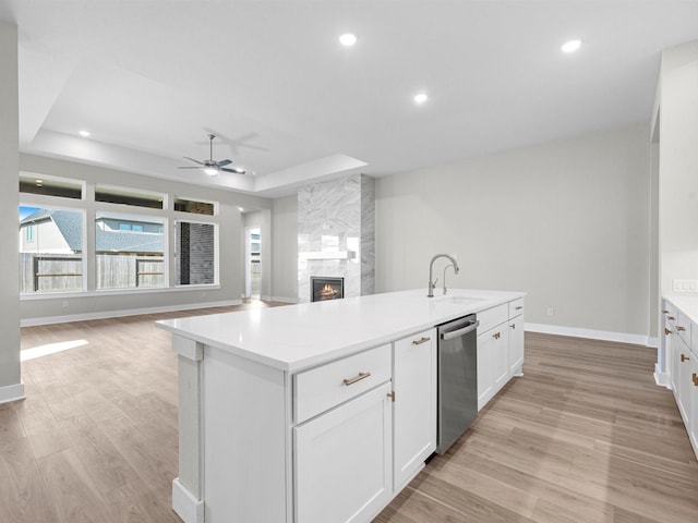 kitchen featuring white cabinets, an island with sink, a fireplace, and a tray ceiling