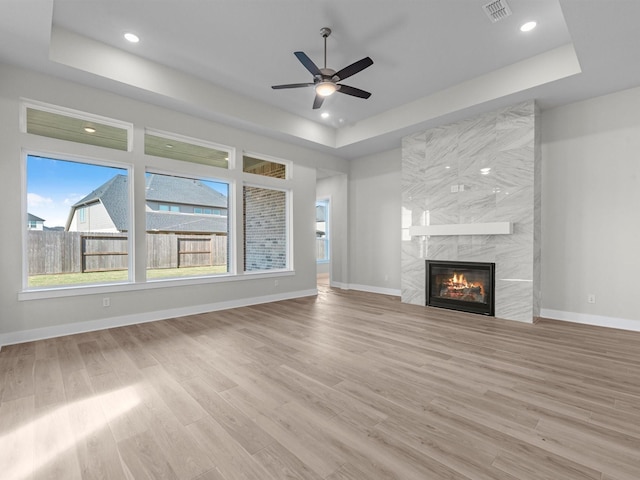 unfurnished living room featuring a tiled fireplace, light hardwood / wood-style floors, and a raised ceiling