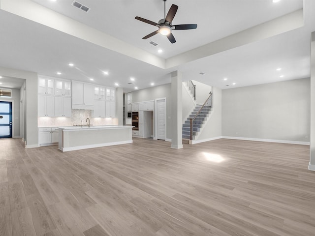 unfurnished living room with light wood-type flooring, ceiling fan, and sink