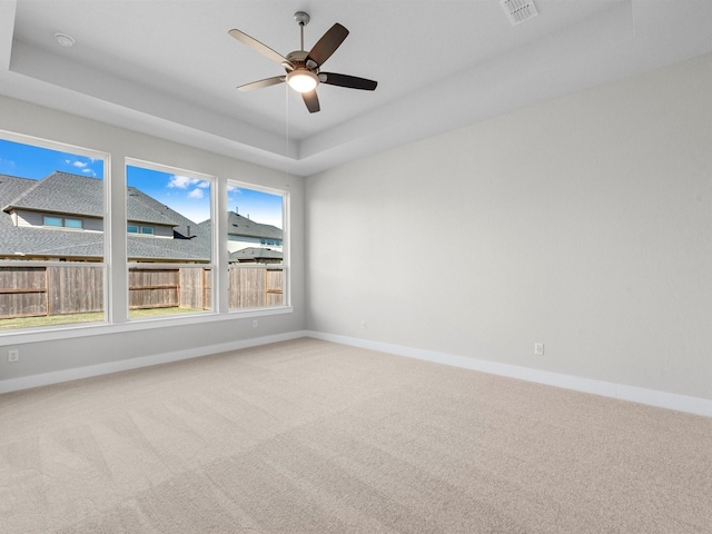 empty room with a raised ceiling, ceiling fan, a wealth of natural light, and carpet flooring