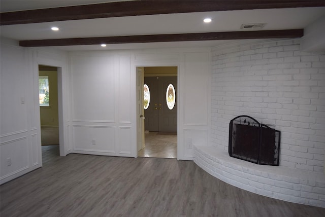 unfurnished living room featuring beamed ceiling, light wood-type flooring, and a brick fireplace