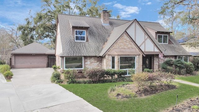 tudor house with a garage, brick siding, roof with shingles, a chimney, and a front yard