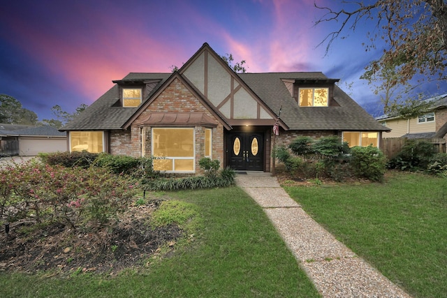 tudor-style house featuring a yard, roof with shingles, stone siding, and stucco siding