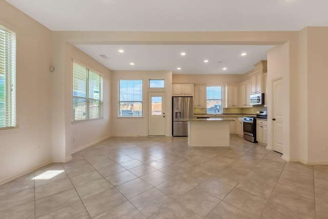 kitchen featuring sink, light tile patterned floors, appliances with stainless steel finishes, cream cabinetry, and a kitchen island