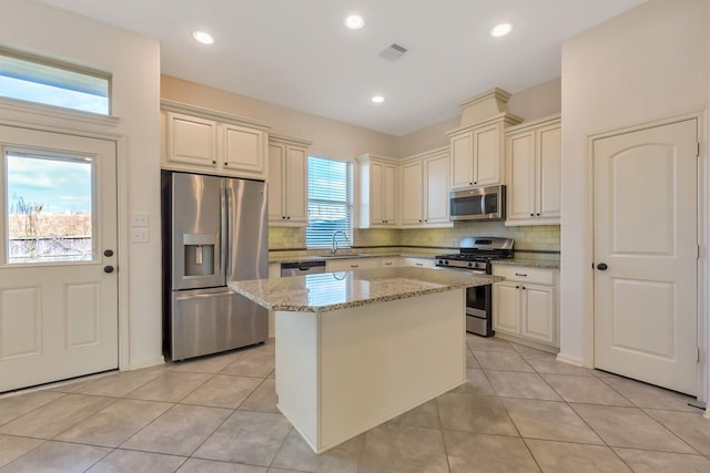 kitchen with a center island, sink, light tile patterned floors, light stone counters, and stainless steel appliances