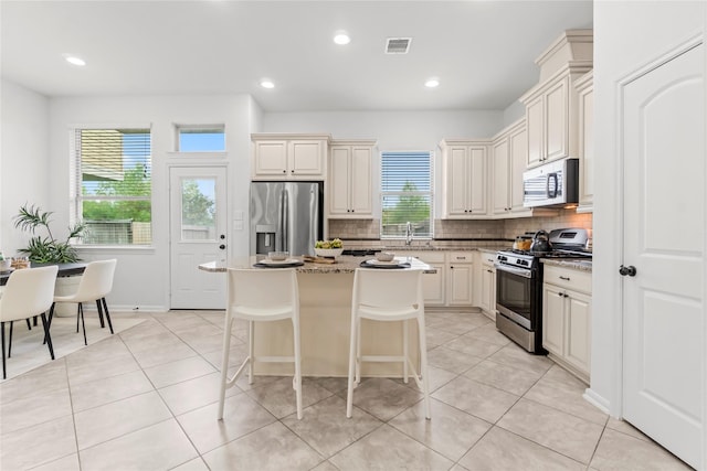 kitchen featuring light stone countertops, stainless steel appliances, light tile patterned floors, a center island, and a breakfast bar area