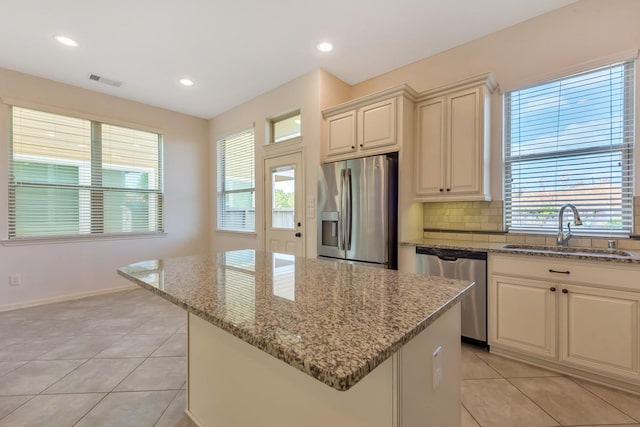 kitchen with light stone countertops, appliances with stainless steel finishes, sink, light tile patterned floors, and a center island