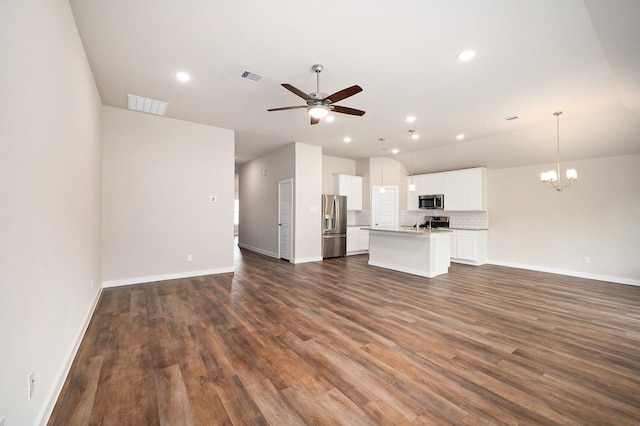 unfurnished living room with ceiling fan with notable chandelier and dark wood-type flooring