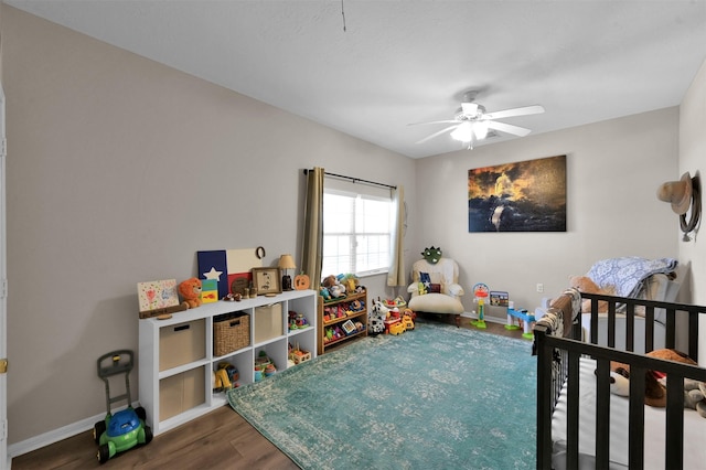 bedroom with ceiling fan, a crib, and dark wood-type flooring