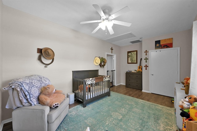 bedroom with a crib, dark hardwood / wood-style floors, and ceiling fan