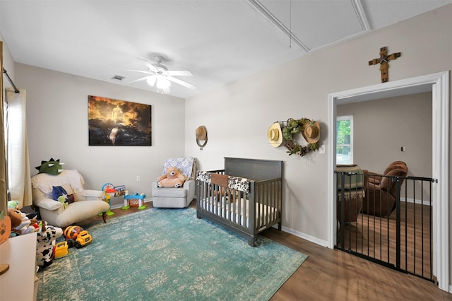 bedroom featuring hardwood / wood-style floors, a nursery area, and ceiling fan