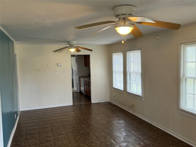 empty room featuring a textured ceiling, wooden walls, ceiling fan, and ornamental molding