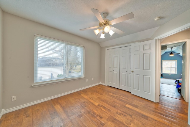 unfurnished bedroom featuring vaulted ceiling, a textured ceiling, a closet, hardwood / wood-style flooring, and ceiling fan