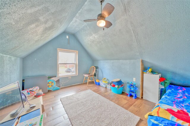 playroom featuring wood-type flooring, vaulted ceiling, ceiling fan, and a textured ceiling