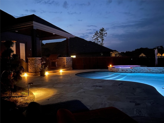 pool at dusk with a patio area and an in ground hot tub