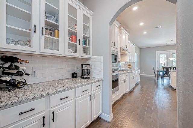 kitchen featuring appliances with stainless steel finishes, tasteful backsplash, light stone counters, hardwood / wood-style floors, and white cabinetry