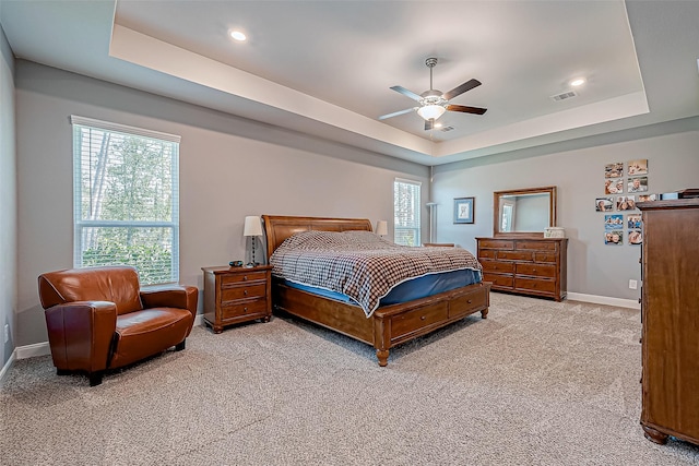 carpeted bedroom with ceiling fan, multiple windows, and a tray ceiling