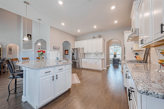 kitchen featuring white cabinets, stainless steel fridge, backsplash, and a kitchen island with sink