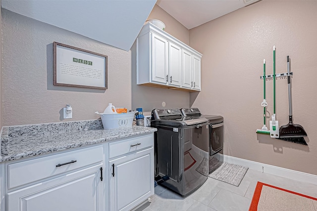 clothes washing area with washer and clothes dryer, light tile patterned floors, and cabinets