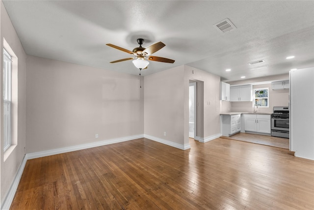 unfurnished living room featuring ceiling fan, sink, a textured ceiling, and light hardwood / wood-style flooring