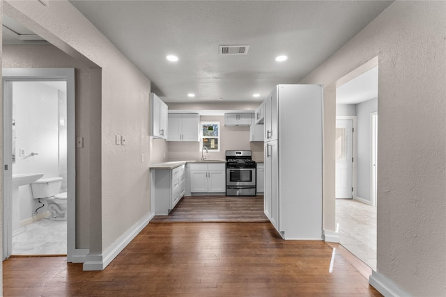 kitchen with dark hardwood / wood-style flooring, white cabinetry, sink, and stainless steel gas range