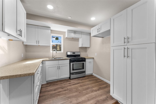 kitchen featuring stainless steel gas stove, light stone countertops, white cabinetry, and sink