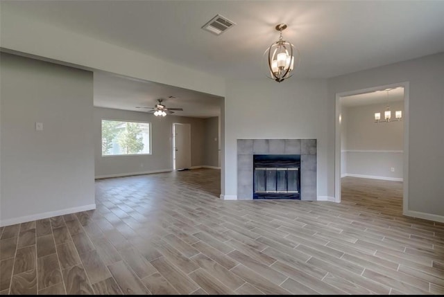 unfurnished living room with a tile fireplace, ceiling fan with notable chandelier, and light hardwood / wood-style floors