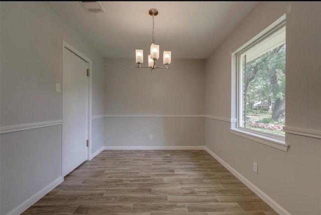 unfurnished room featuring plenty of natural light, a chandelier, and light hardwood / wood-style flooring